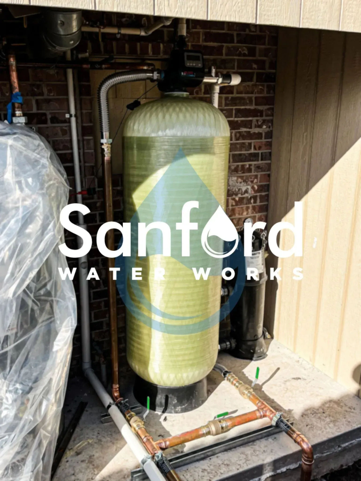 Water filtration system installed outdoors near a brick wall and siding.