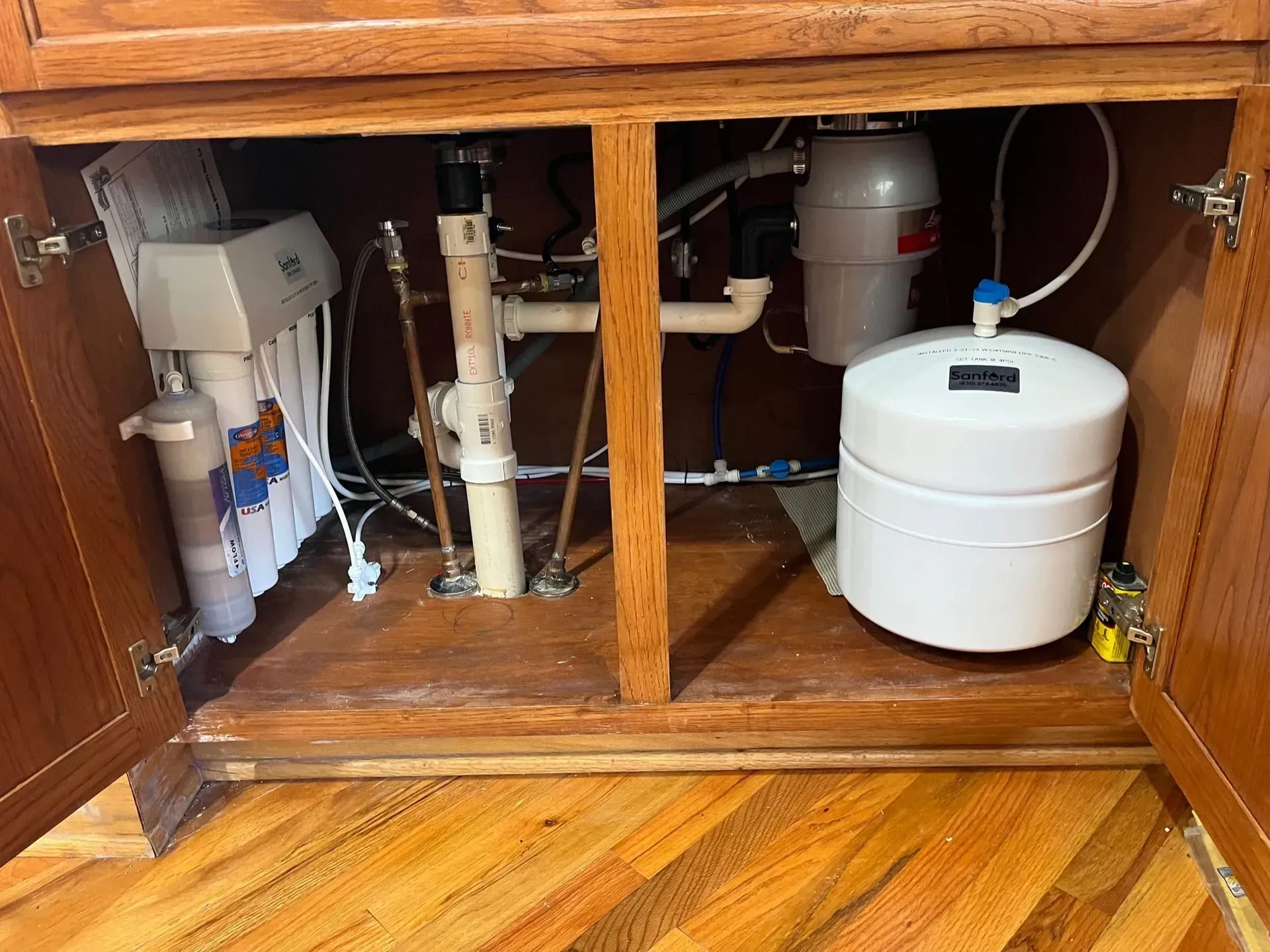 Kitchen cabinet interior with plumbing, water filter, and garbage disposal.
