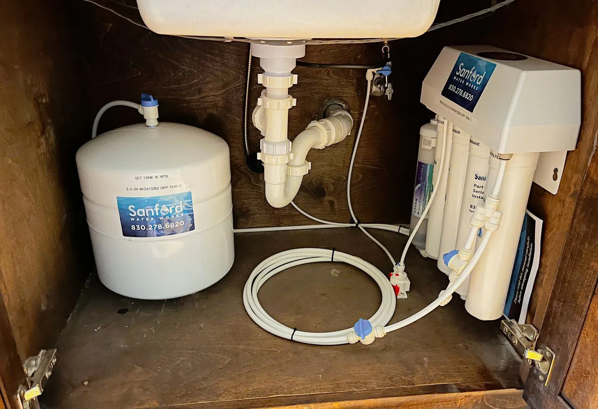 Under-sink water filtration system with white tank, filter unit, and hoses in a cabinet