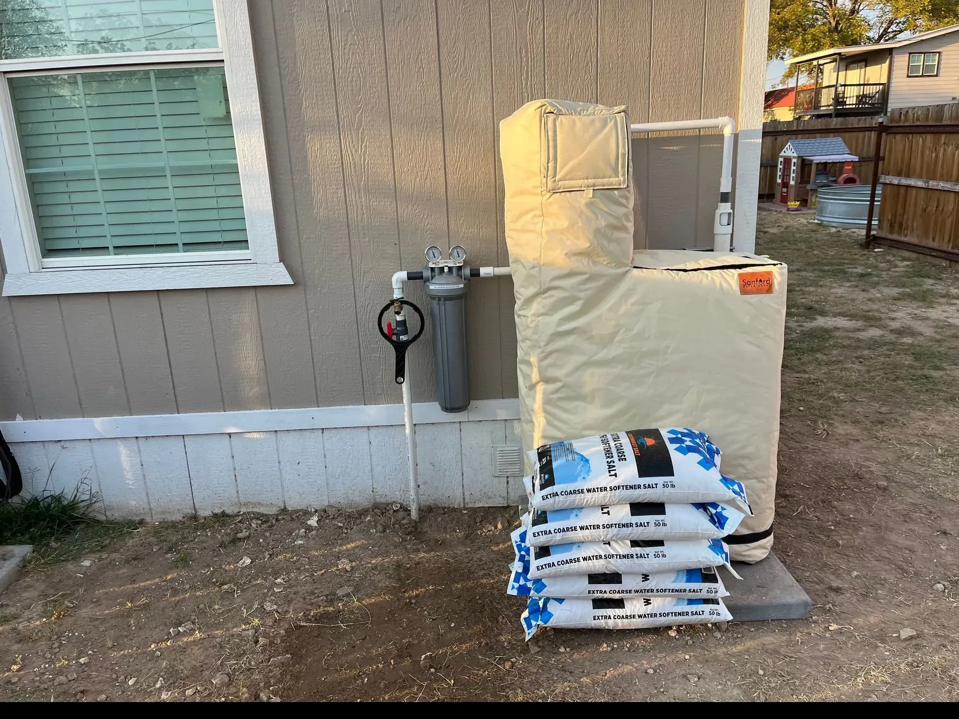 Exterior view of a building with a water filter, insulated water heater, and bags of water softener salt.