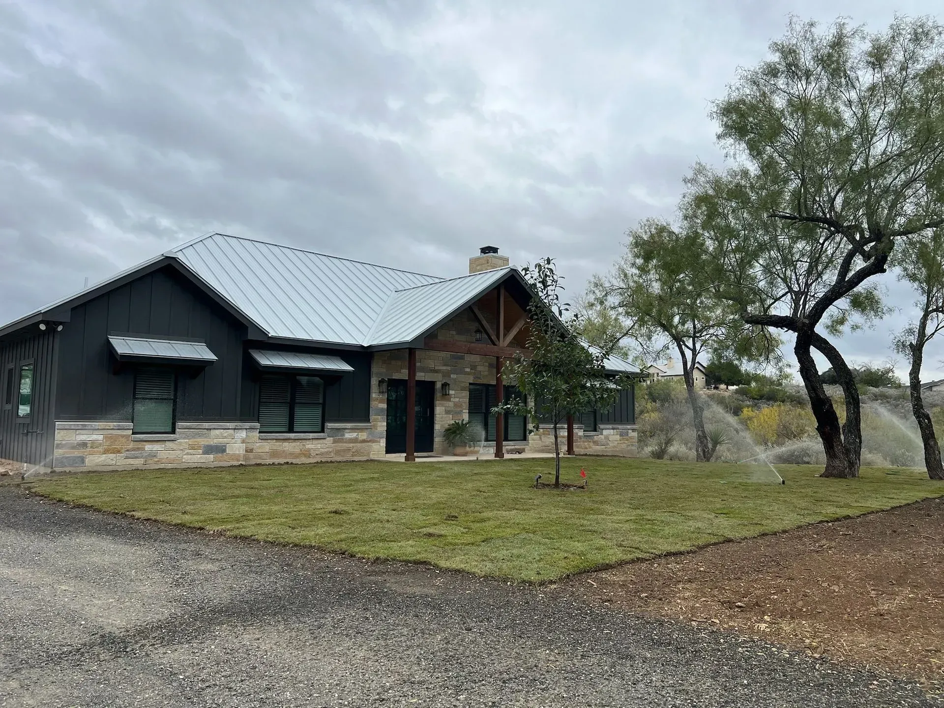 Gray house with metal roof and stone facade, overcast day.