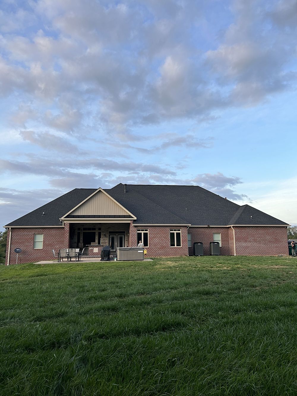 A large brick house with a black roof is sitting on top of a lush green field.