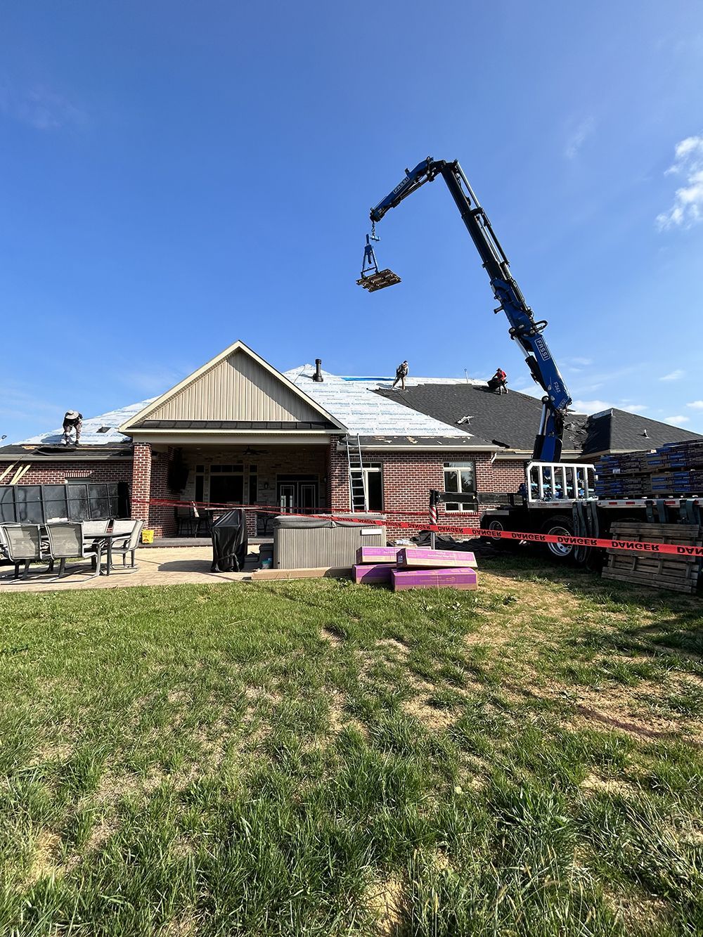 A crane is lifting a roof over a house.