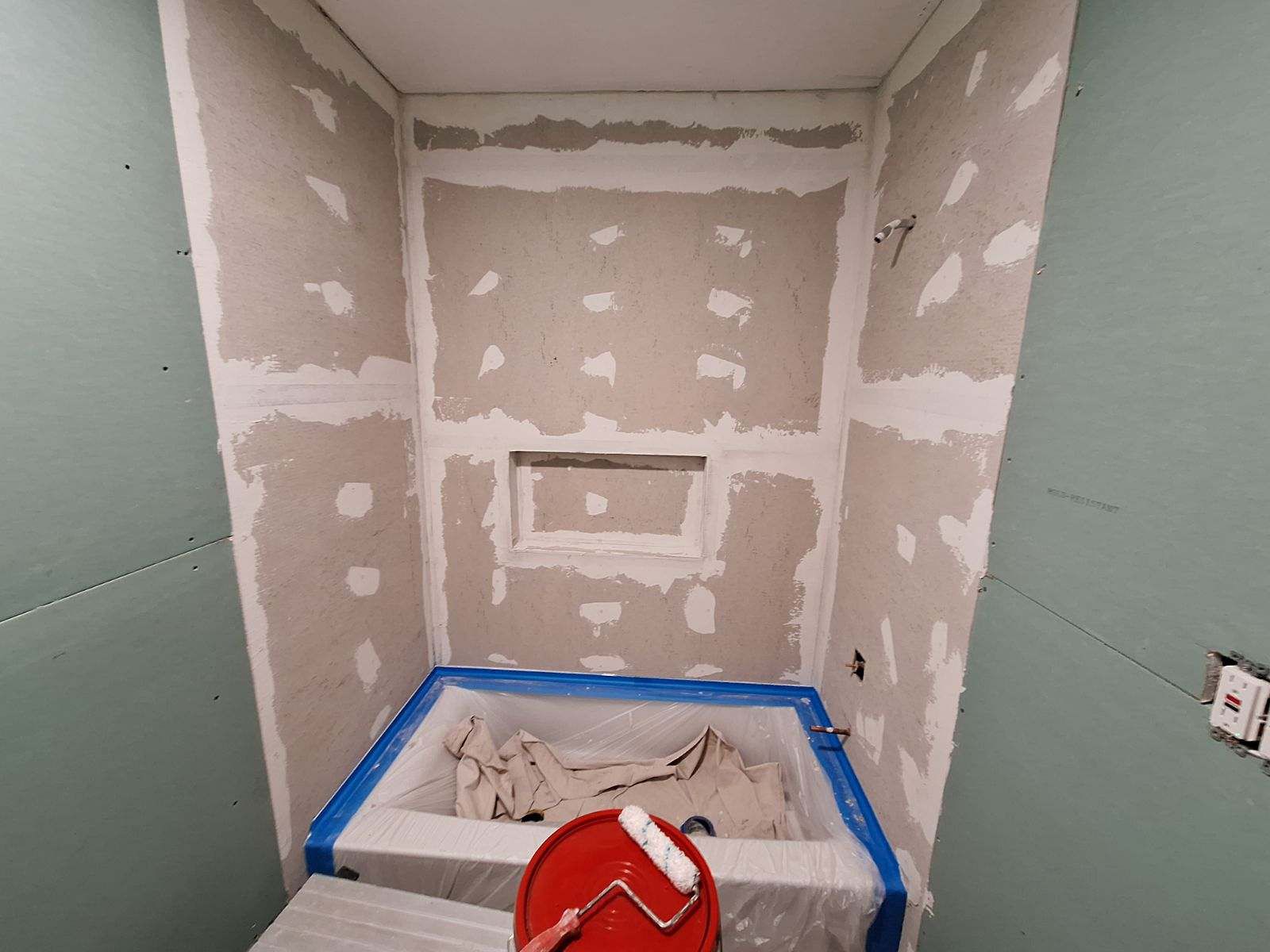 A bathroom under construction with a bucket of paint and a roller.