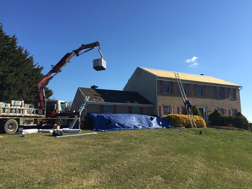 A crane is lifting a piece of wood in front of a house.