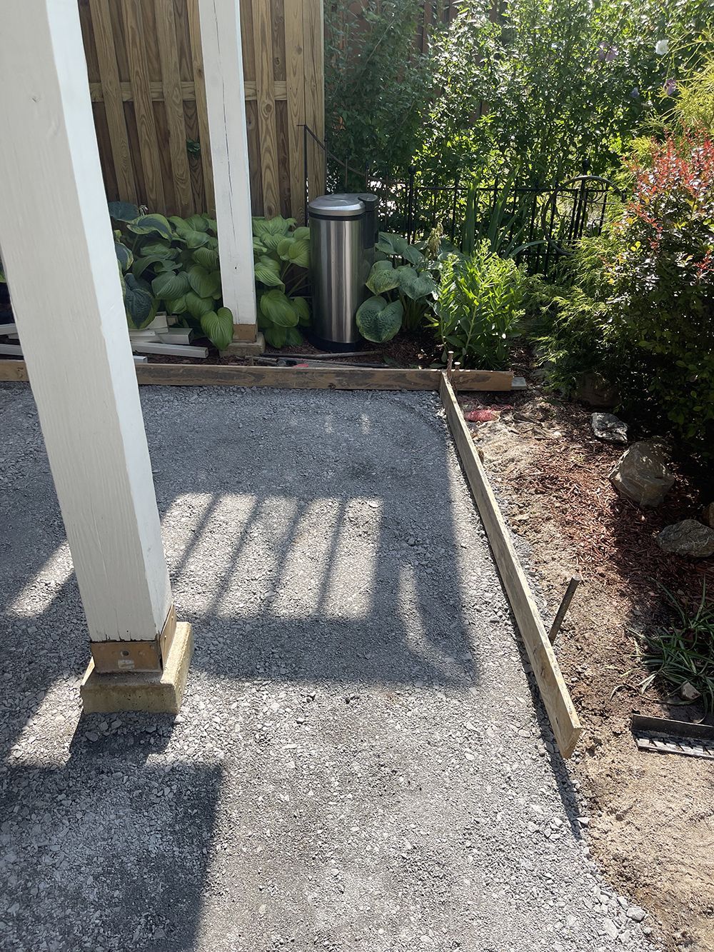 A trash can is sitting in the middle of a gravel driveway.
