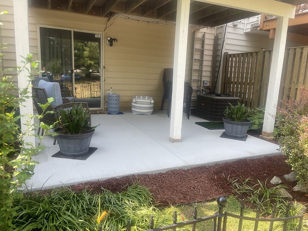 A patio with potted plants and chairs under a covered porch.