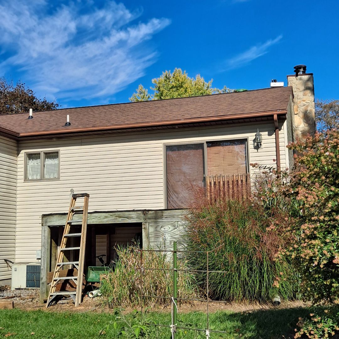 A white house with a brown roof and a ladder in front of it.