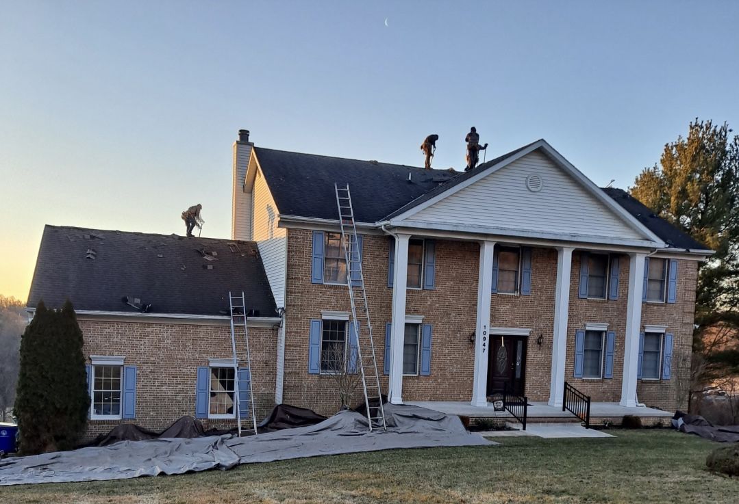 Two men are working on the roof of a large brick house.
