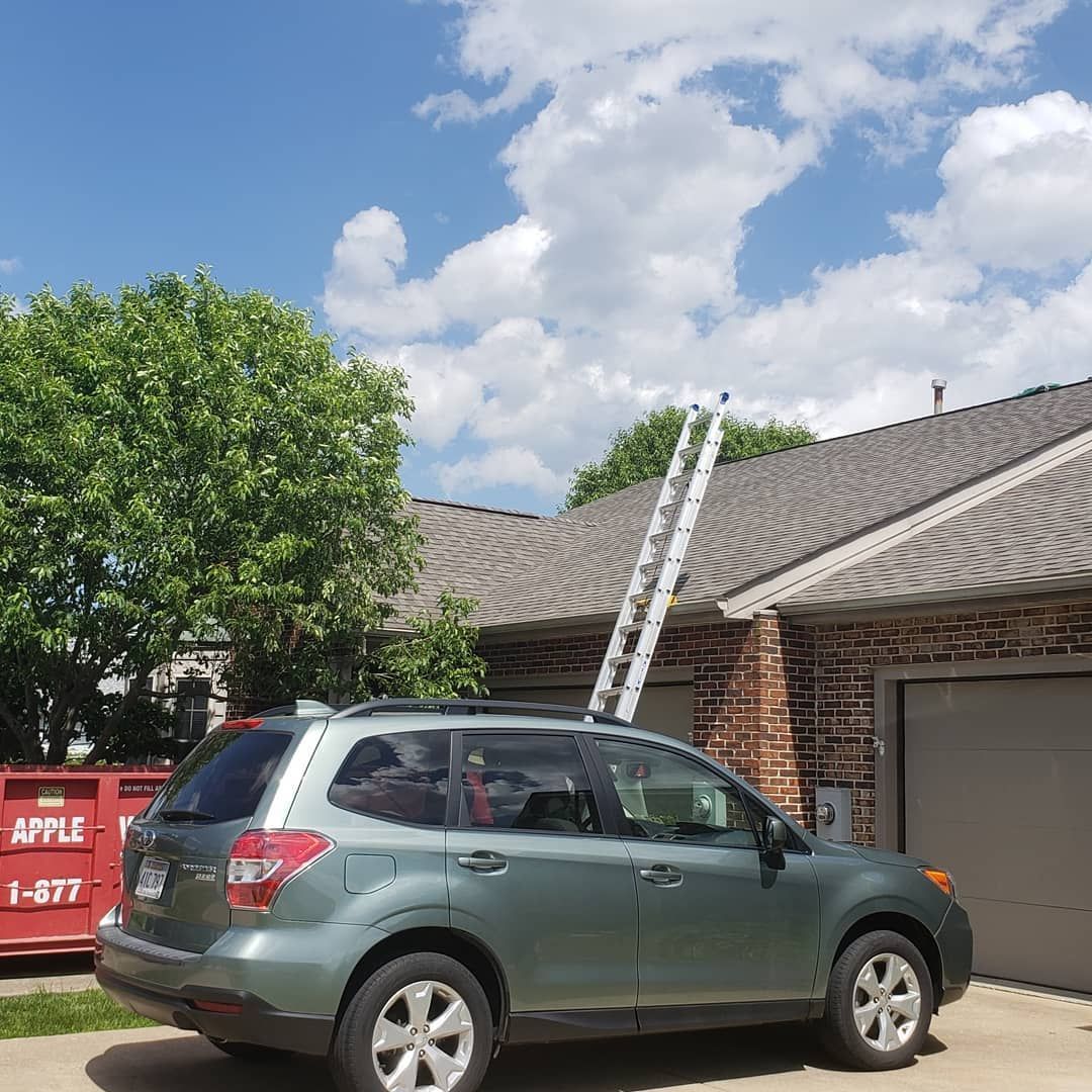 A car is parked in front of a house with a ladder on the roof.