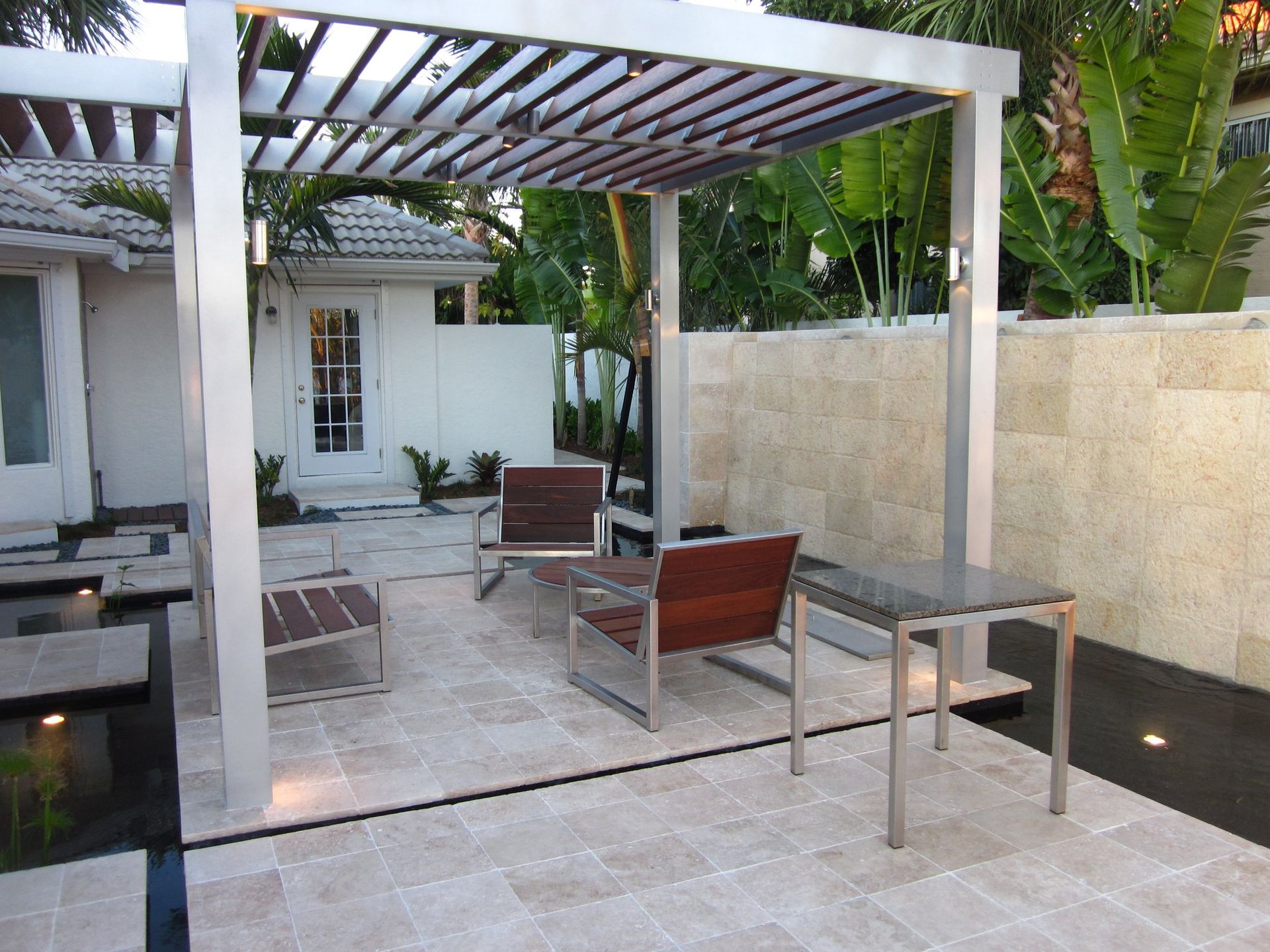 Patio with modern furniture under a metal pergola; stone patio, neutral color scheme.