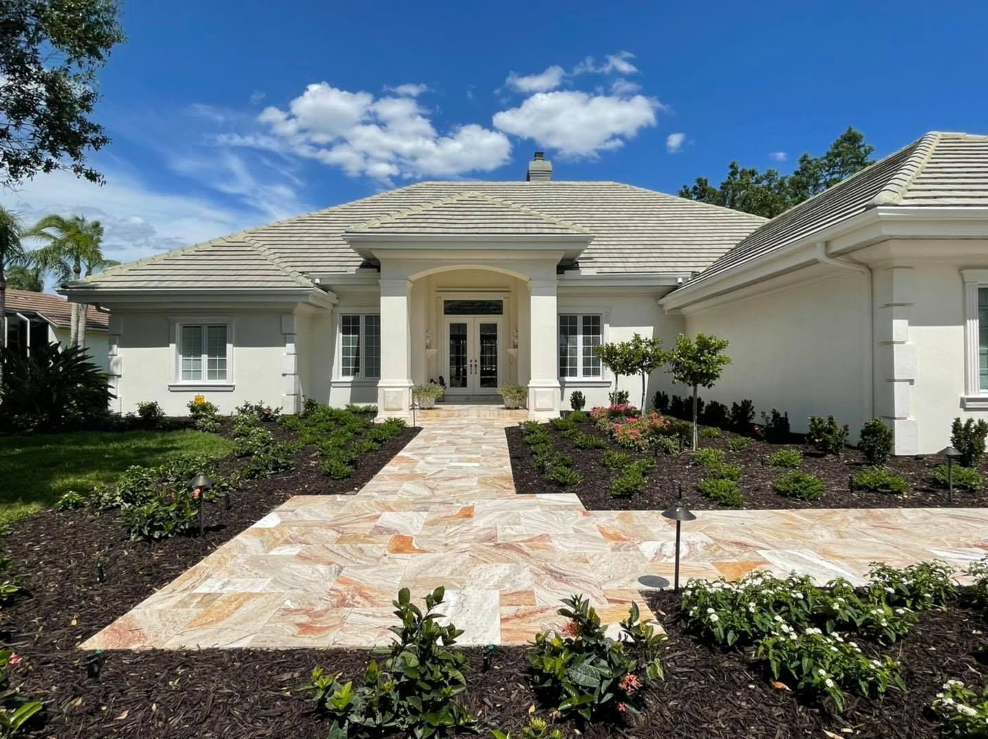 A one-story white house with a stone path leading to the front door, surrounded by landscaping under a blue sky.
