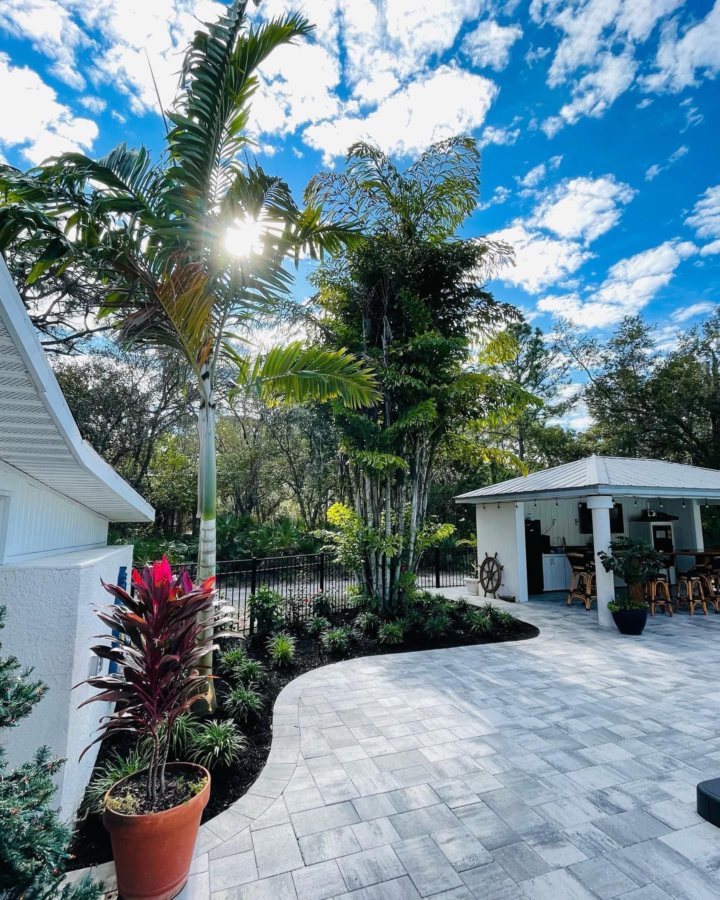 Palm trees and lush landscaping in a bright yard with a white cabana on a sunny day.