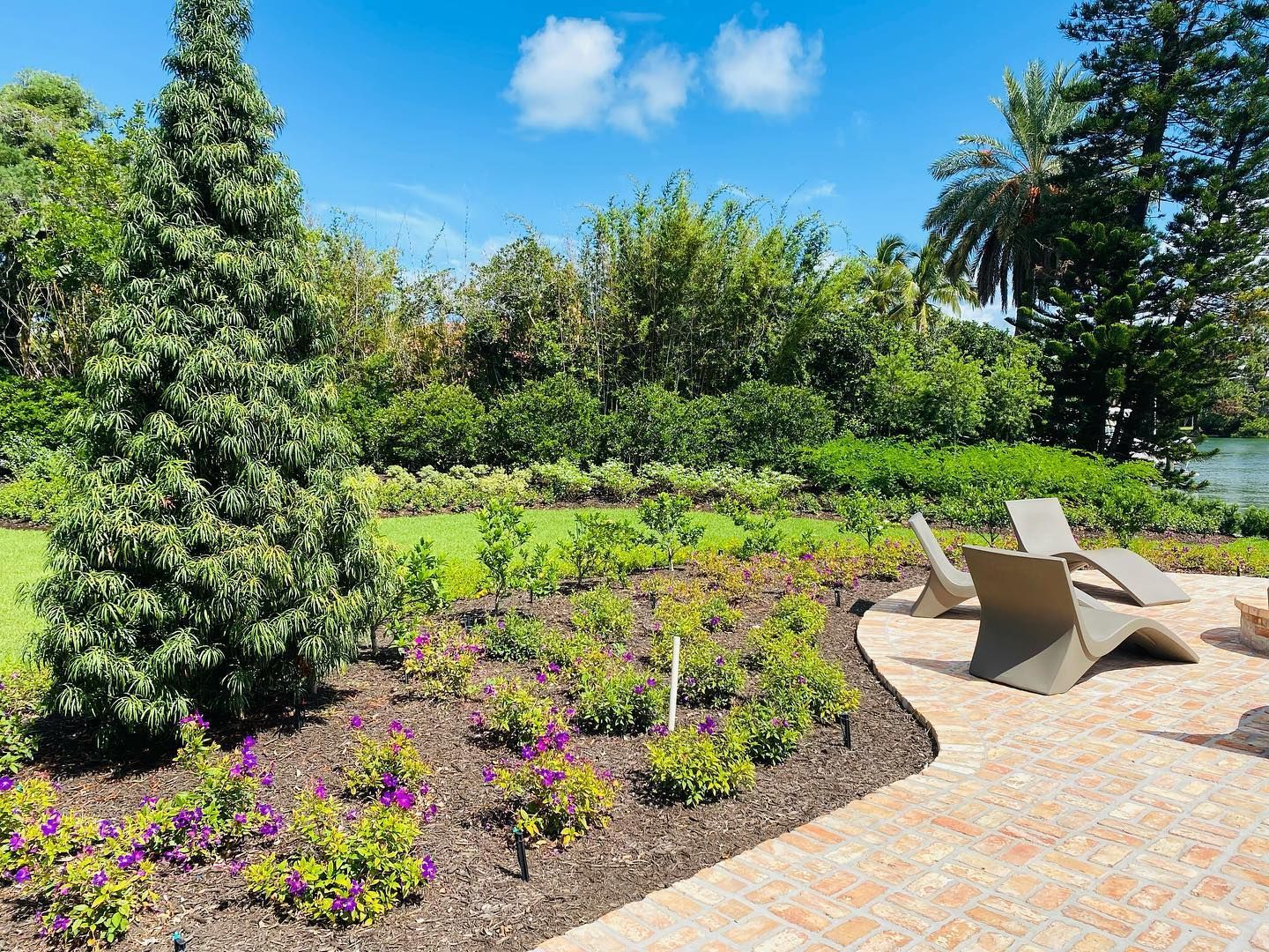 Lush garden with lounge chairs on a patio, overlooking greenery and blue sky with clouds.