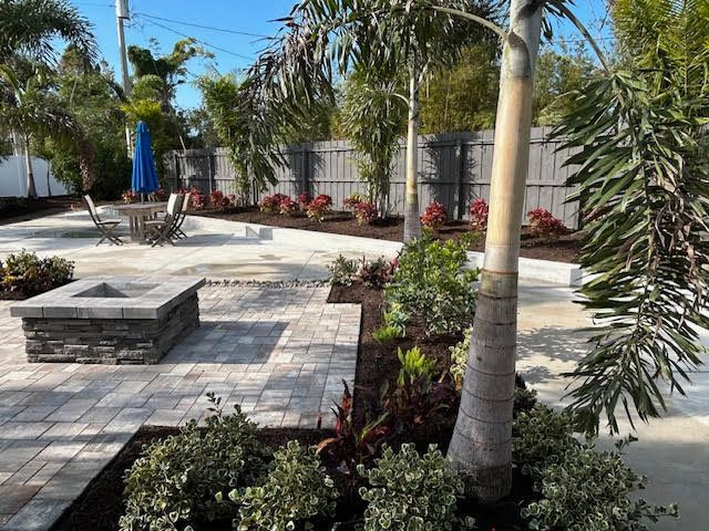 Landscaped backyard with pavers, fire pit, seating area, and palm trees.