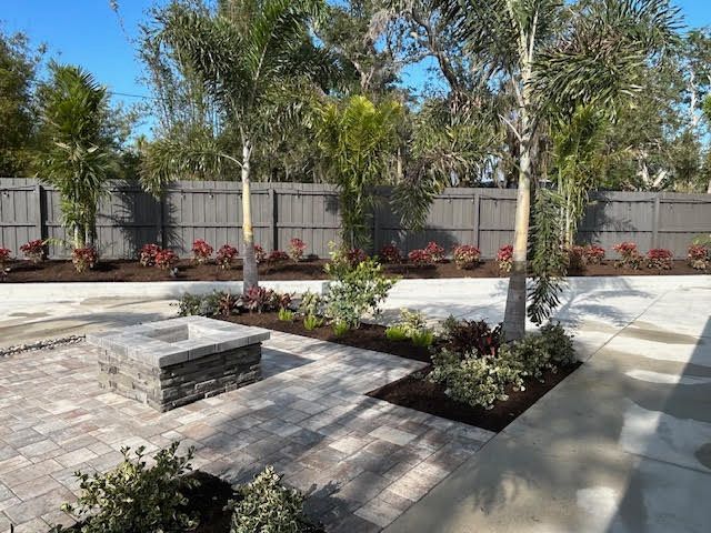 A backyard patio with a fire pit, palm trees, and a gray wooden fence.