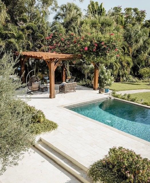 Poolside pergola with flowering vine, adjacent to pool and lush garden.