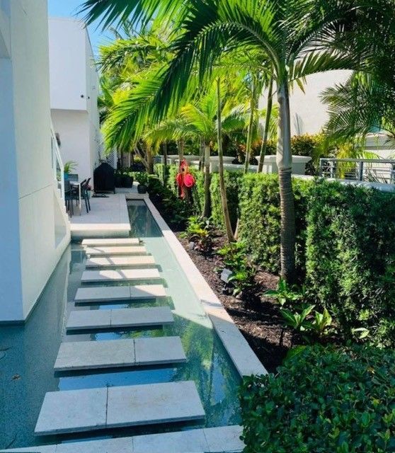 Stone path over water feature with palm trees and manicured landscaping alongside a modern building.