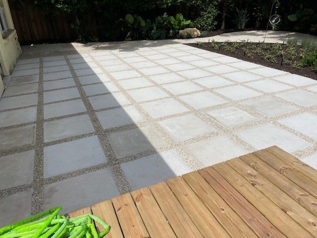 Patio with square concrete pavers and gravel joints next to a wooden deck.