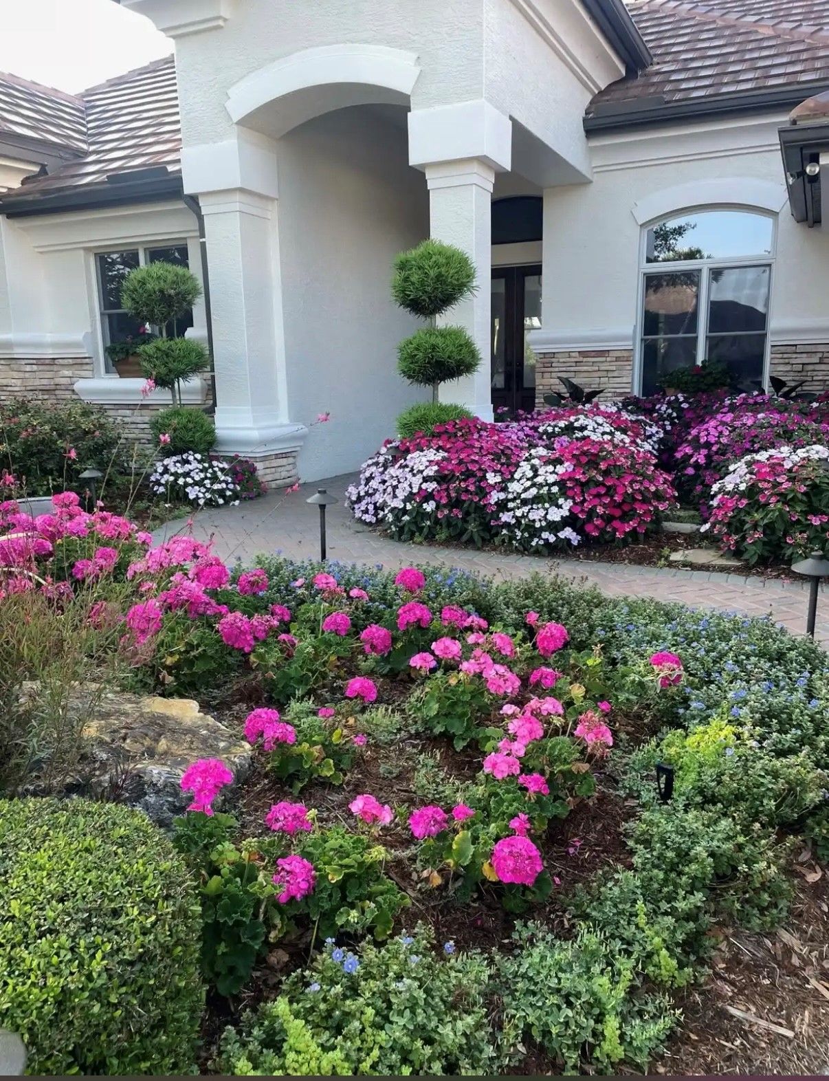 Exterior of a house with a landscaped garden featuring pink, white, and purple flowers along a stone pathway.