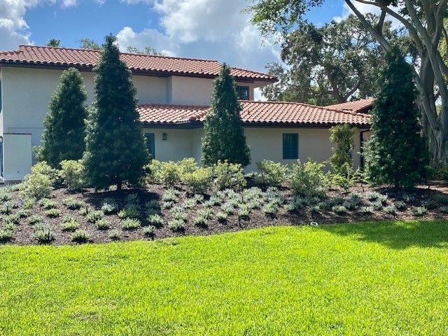 A house with a terracotta roof and landscaping, featuring trees and shrubs, on a grassy lawn.