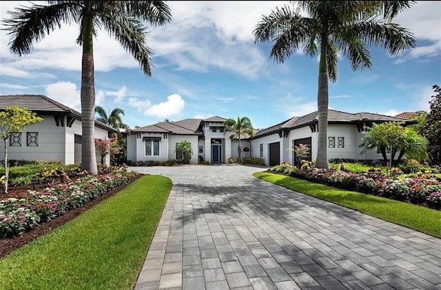 Modern home with palm trees, long driveway, and well-maintained landscaping under a blue sky.