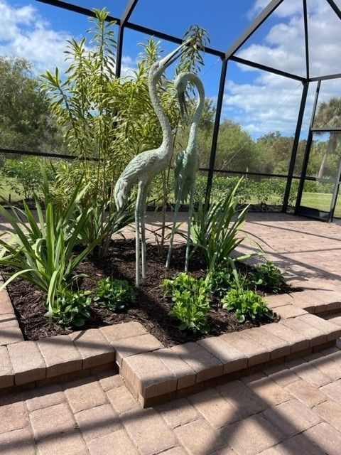Two metal crane sculptures in a landscaped outdoor enclosure with brick pavers.