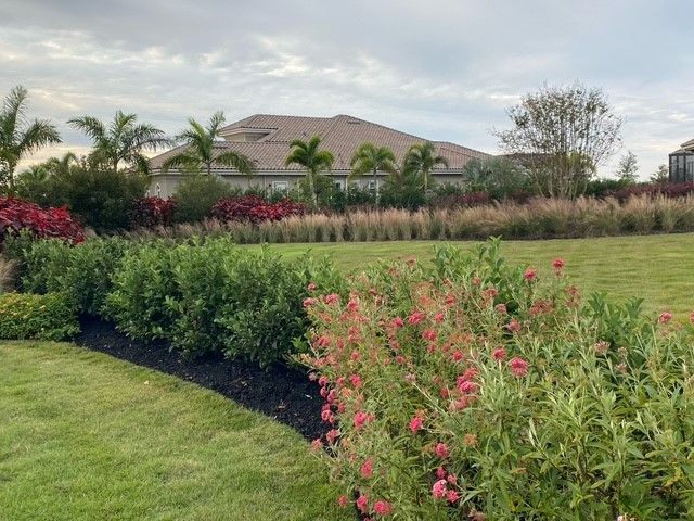 Lush green lawn and flowerbeds lead to a house under a cloudy sky.