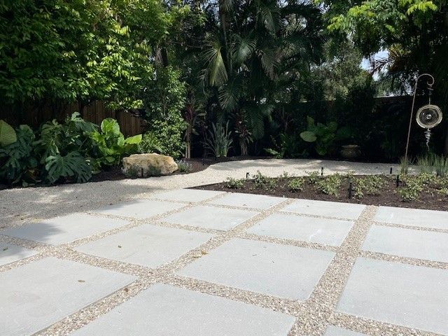 Concrete patio with gravel in between, surrounded by lush green landscaping and plants.