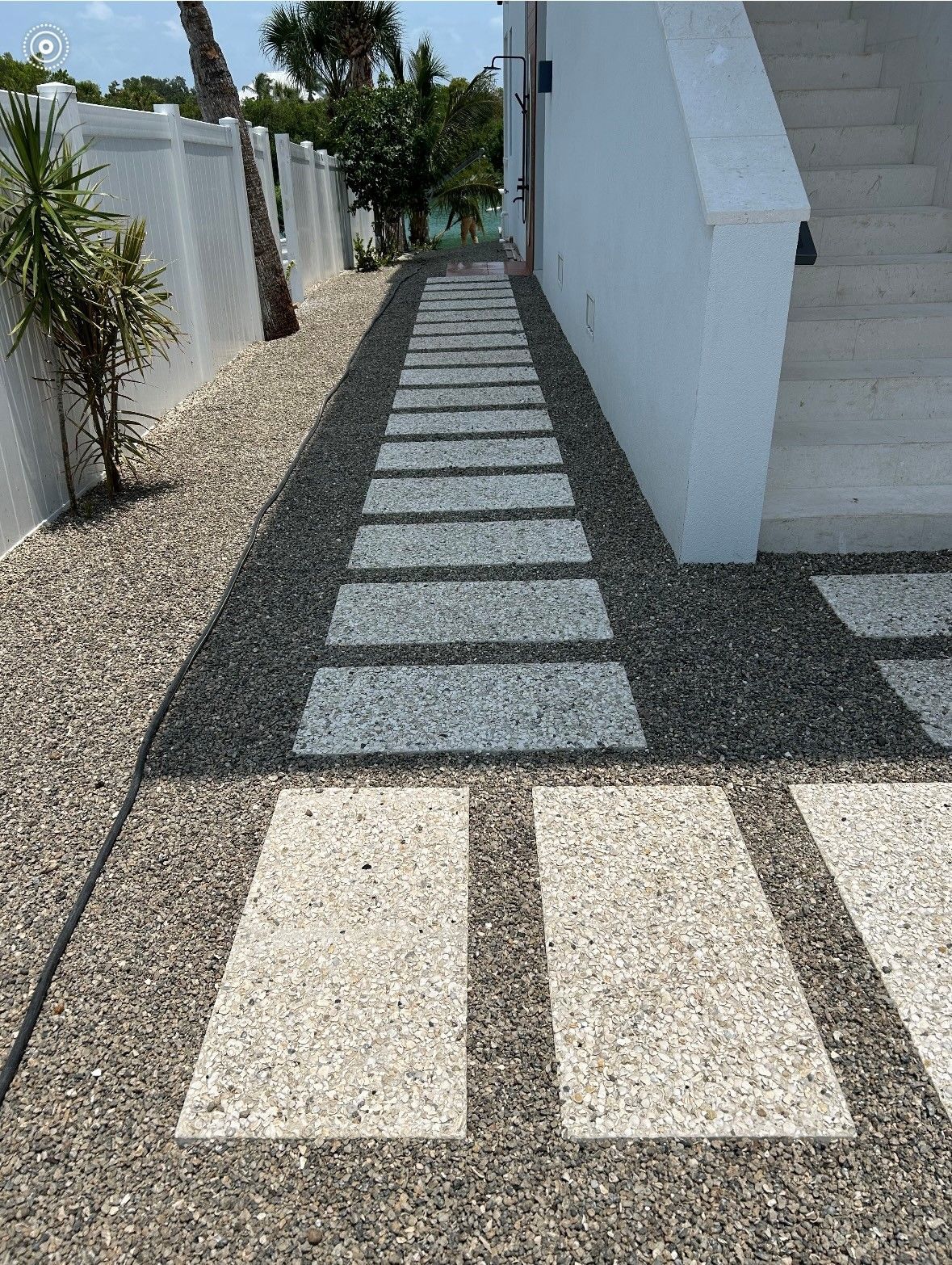 Stone pathway lined with gravel leads to steps beside a white building.