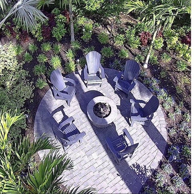 Aerial view of Adirondack chairs around a fire pit on a brick patio, surrounded by plants.