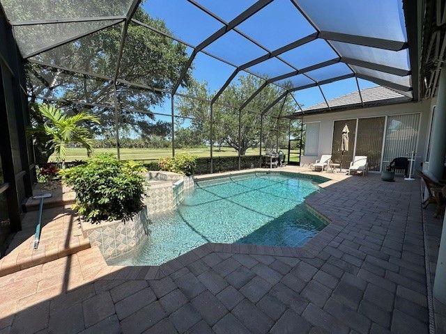 Screened-in pool area with a pool, landscaping, and a view of trees and a golf course on a sunny day.