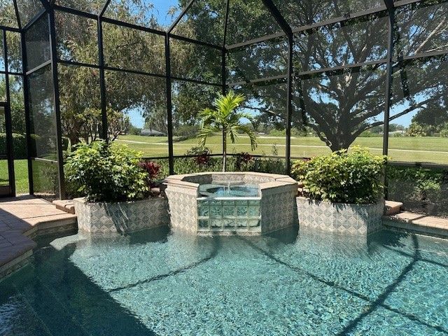 Pool area with hot tub, surrounded by screen enclosure, plants, and a golf course view.