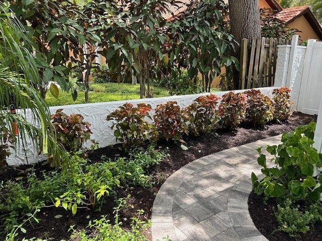 A curved stone path winds through a garden with a white wall and burgundy shrubs.
