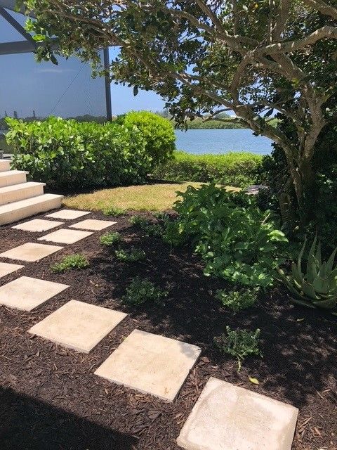 Stone path leads through garden with greenery to water view.