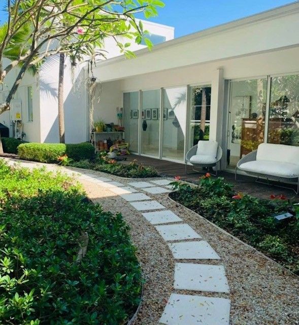 Stone path leads through a garden to a white building with seating.