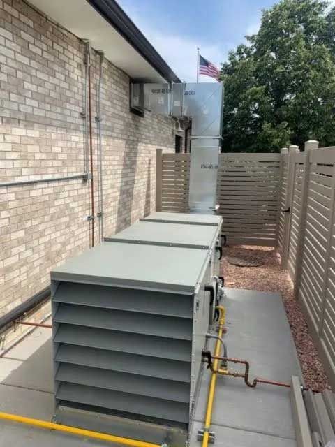 HVAC units outside a brick building, partially screened by beige fencing. An American flag is visible.