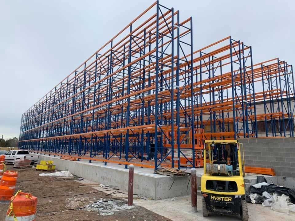 Construction site with large, blue and orange industrial shelving; a forklift is in the foreground.