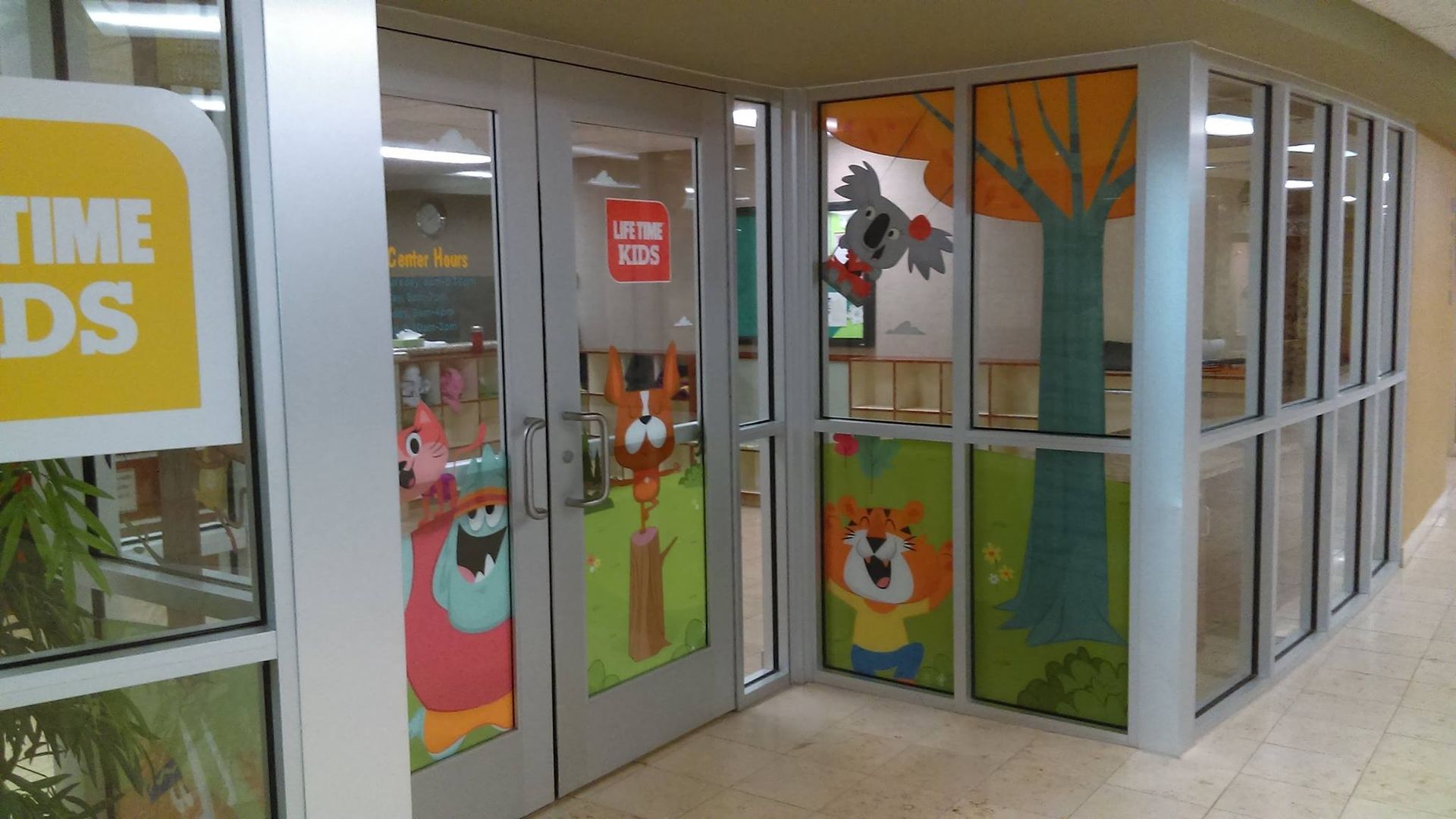 Entrance to a children's area with cartoon animal decals on the glass doors and windows, a forest scene.