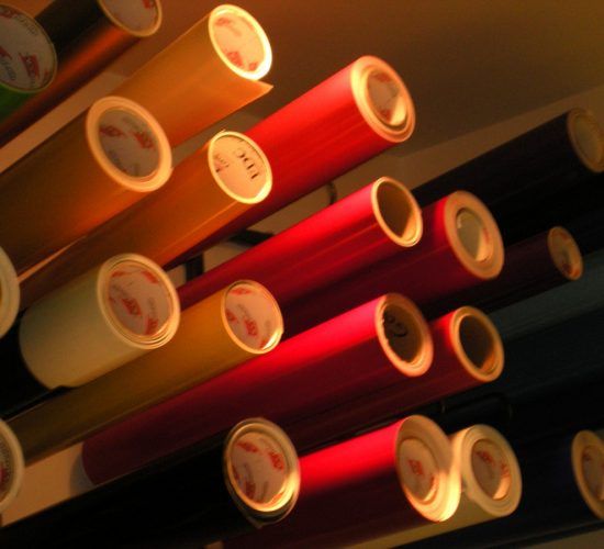 Rolls of colorful vinyl material, various colors, stacked on shelves.