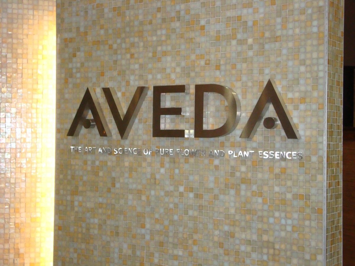 Aveda logo on a mosaic tile wall, featuring the brand name in metallic letters and text below.
