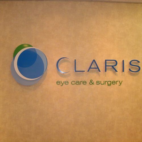 Claris eye care & surgery logo: blue and white circles with text on a beige wall.