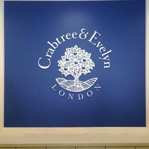 Crabtree & Evelyn logo: white text and tree emblem on blue wall, 