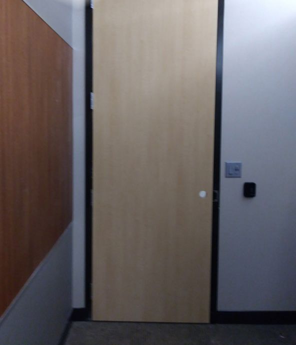 Beige door in a gray doorway with black trim, a security panel, and a wall of wood.