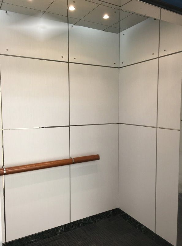 Elevator interior with white paneled walls, a wooden handrail, and a dark floor.