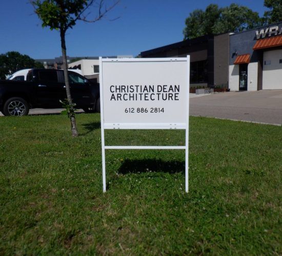 White sign for Christian Dean Architecture on a lawn, next to a black truck and building.