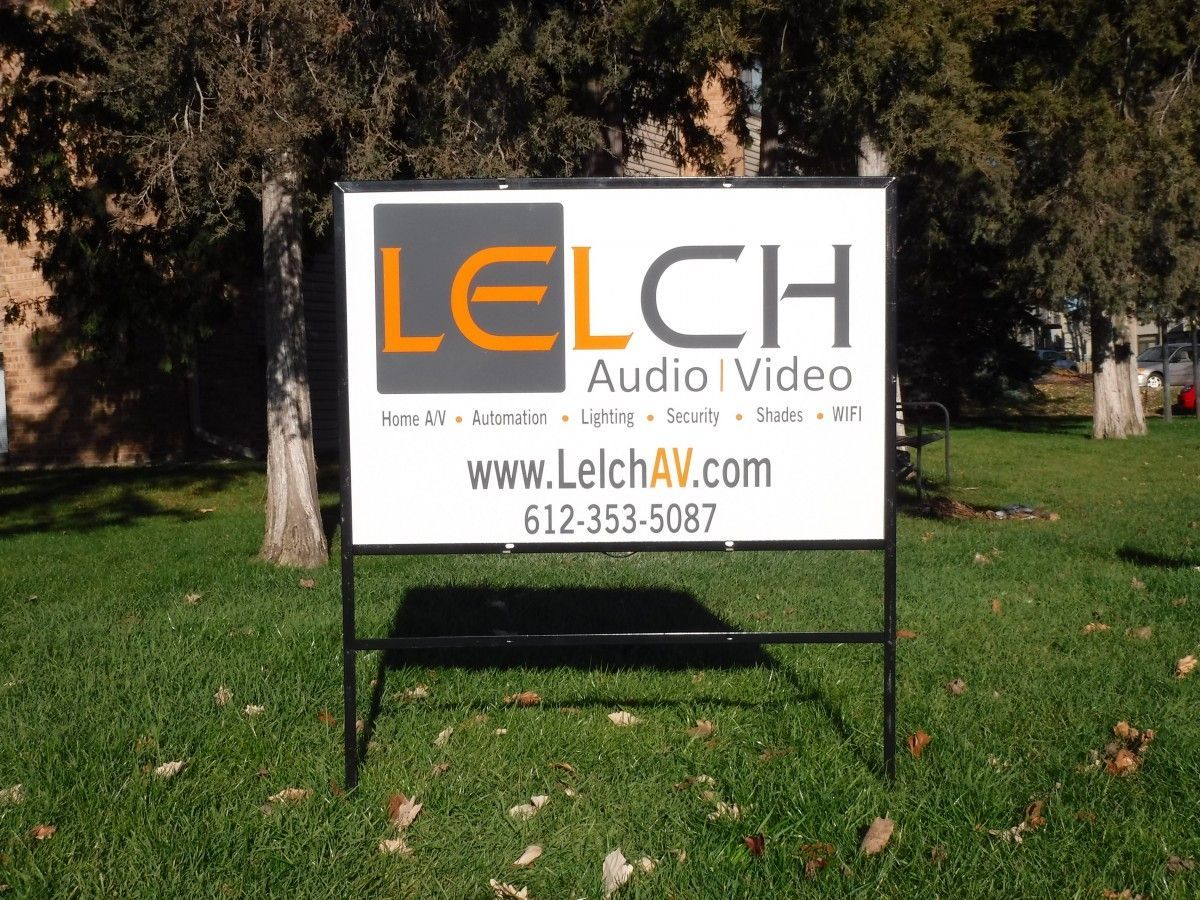 Sign for LELCH Audio | Video on a lawn, black frame, white background, orange and grey logo.