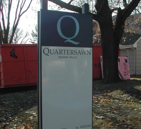 Sign for Quartersawn Design Build with a large "Q" logo and a red dumpster in the background.