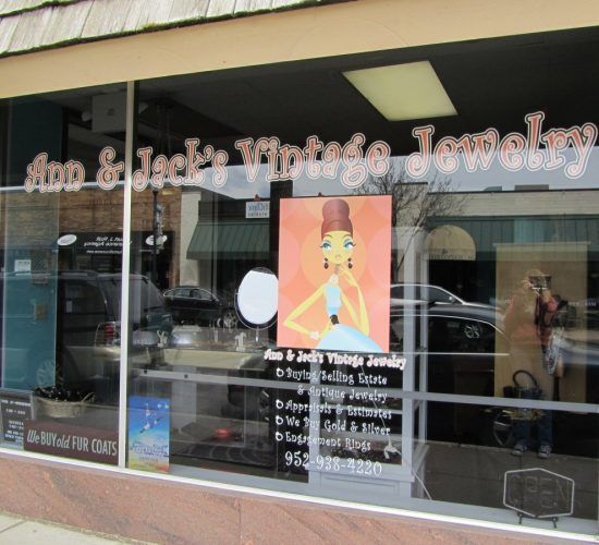 Ann & Jack's Vintage Jewelry storefront with window display. Signage and colorful image of woman wearing jewelry.