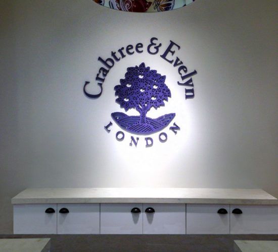Crabtree & Evelyn London logo on a wall above white cabinets. The logo is a purple tree.